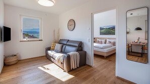 Een moderne woonkamer met een bank, een bed, een eethoek en een grote spiegel.