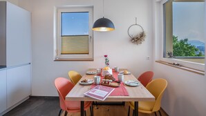 Een eetruimte met een tafel voor vier personen, stoelen, een hanglamp, een raam met uitzicht en een decoratie aan de muur.