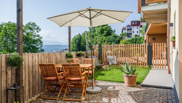 Een terras met tuinmeubilair, een tafel en een parasol.