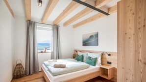 A bedroom with a wooden bed, a nightstand, a window with curtains, and a view of the outdoors. - Holiday Apartment 'Meine Bleibe - Olive' with Mountain View, Garden & Wi-Fi (Eppan an der Weinstraße)