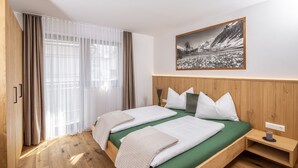 A double bed with a green bedspread, wooden headboard, and a nightstand with a lamp. - Apartment 'Zum Sonnentor - Larix' with Mountain View, Balcony & Wi-Fi (Luttach)