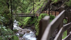A wooden bridge over a flowing river in a forested area. - Apartment 'Zum Sonnentor - Larix' with Mountain View, Balcony & Wi-Fi (Luttach)