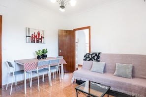 A living room with a sofa, a dining table with chairs, a coffee table, and a door leading to another room.