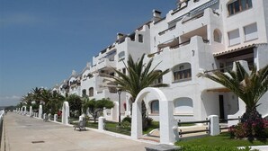 Una hilera de edificios blancos con balcones, un paseo empedrado y palmeras.