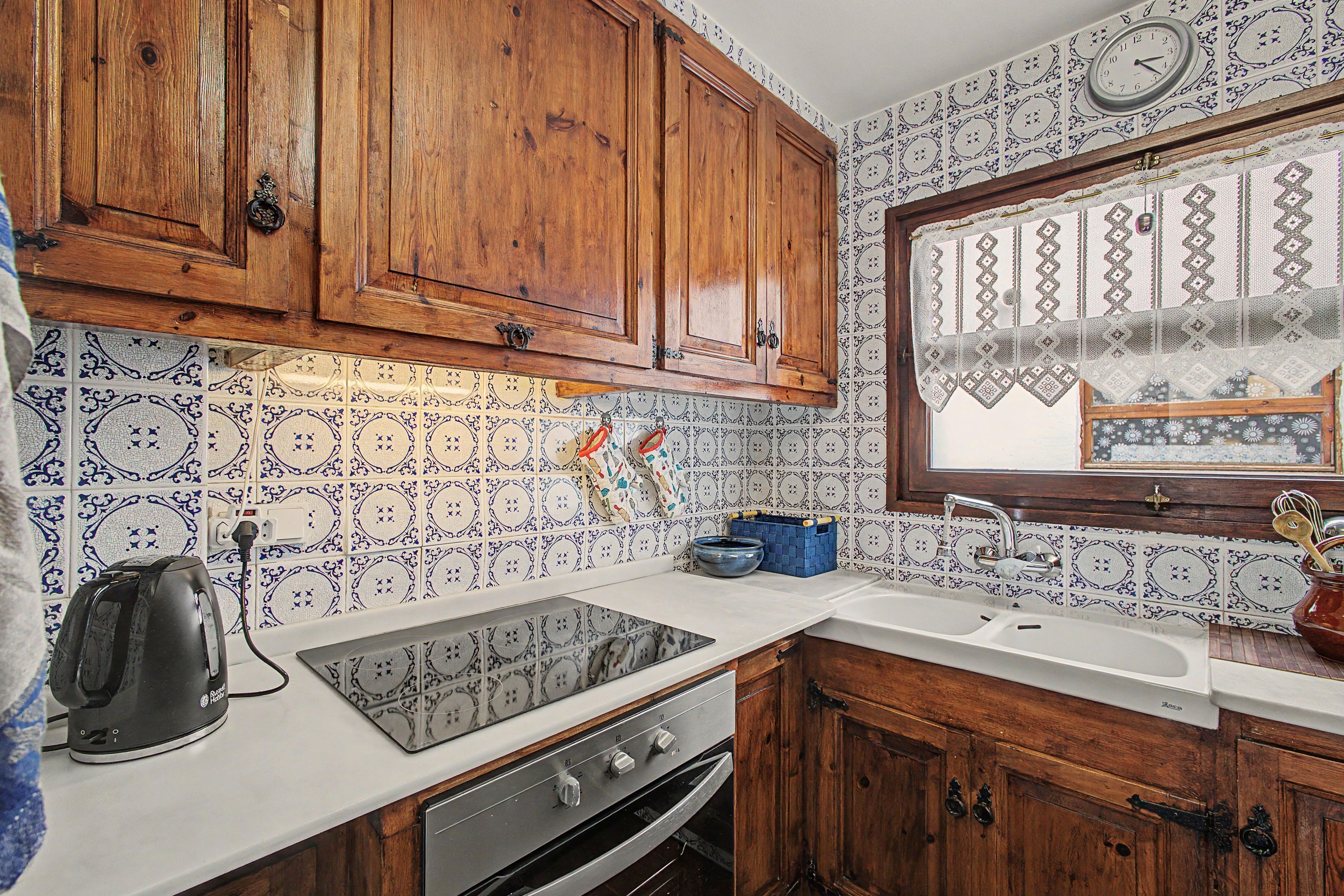 Une cuisine avec des meubles de rangement en bois, une cuisinière, un évier et des carreaux décoratifs.
