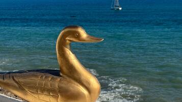 Une sculpture dorée représentant un oiseau au bord de la mer, avec un voilier en arrière-plan.
