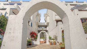 Un patio con un arco central, plantas en macetas y suelo de baldosas.