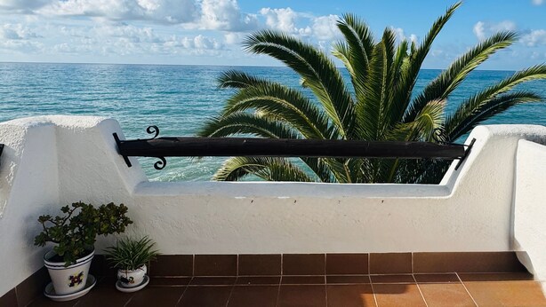 Un balcón con barandilla, plantas en macetas y vista al mar.