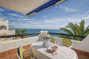 A terrace with a table, chairs, a potted plant, and a view of the sea. - Apartment 'Sea Breeze' with Terrace, Shared Garden & Wi-Fi (Vilanova i la Geltrú)