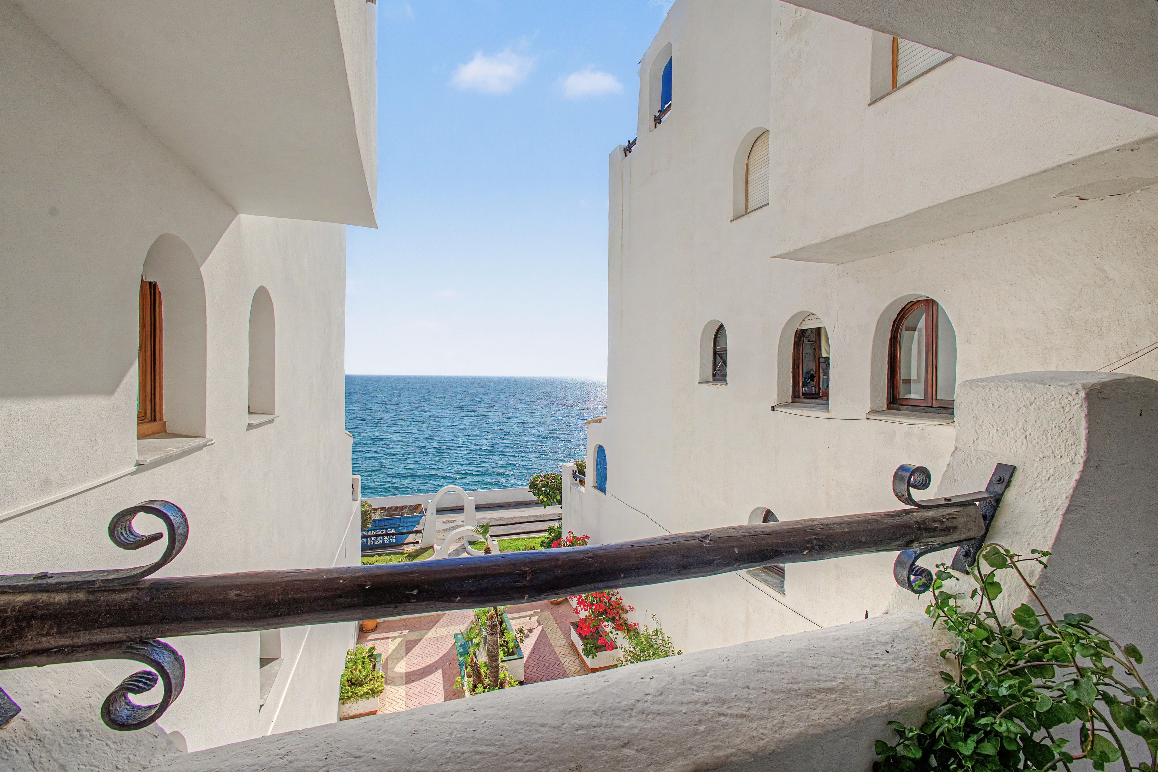 Un balcon avec vue sur la mer, des bâtiments blancs et une balustrade en bois.