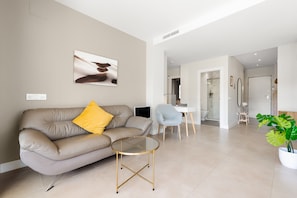 Un salon moderne comprenant un canapé, une table basse en verre, un coin repas et une salle de bain visible à travers une porte ouverte.