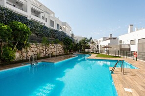 Una piscina con un muro in pietra e vegetazione su un lato, e un edificio con balconi sull'altro.