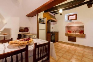 A kitchen with a dining table, chairs, a hanging light bulb, a built-in oven, and a tiled floor.
