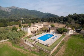 A villa with a swimming pool, surrounded by a garden and a view of mountains.