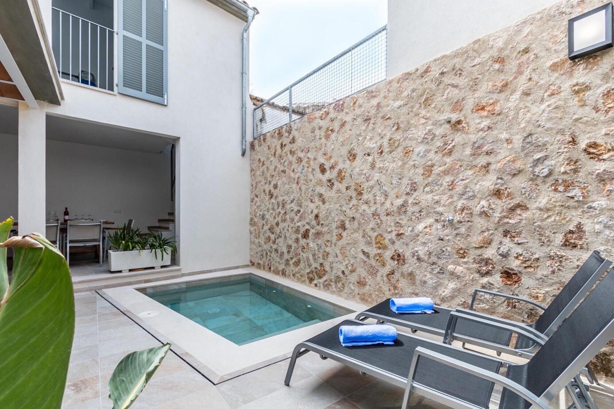 A pool area with lounge chairs, a stone wall, and a staircase leading to an upper level.