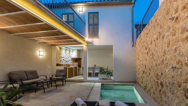 A modern outdoor living area with a pool, seating, and a kitchen visible through an open door. - Vacation Home 'Casa Bugera' with Pool, Balcony, A/C & Wi-Fi (Pollenca)