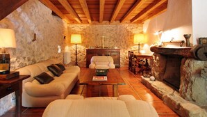 Une pièce chaleureuse avec un mur en pierre, des poutres en bois au plafond, une cheminée et un canapé.