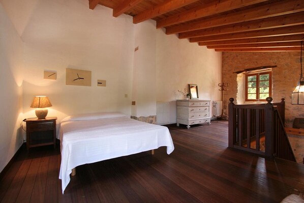 A bedroom with a wooden ceiling, a bed, a dresser, a nightstand, and a window.