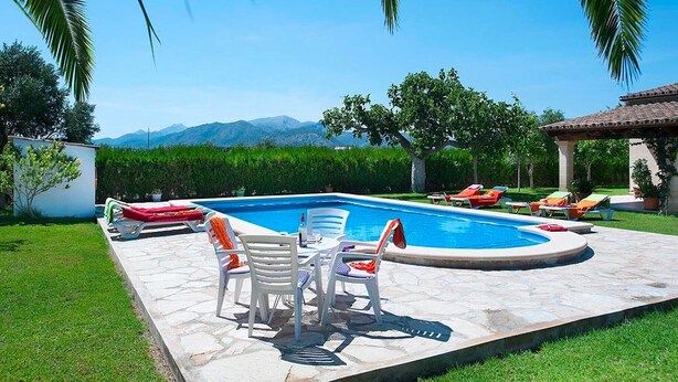 A swimming pool with lounge chairs and a table, surrounded by greenery and a view of mountains. - Finca Villa Burgues with Mountain View, Pool, Garden, Terrace & Wi-Fi (Alcudia)