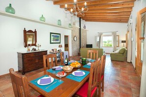 Un coin repas avec une table en bois dressée pour quatre personnes, un lustre et une vue sur le salon.