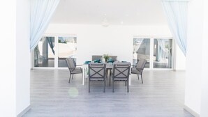 A spacious dining area with a table set for four, surrounded by chairs, large windows with curtains, and a view of the outdoors. - Casa Rural "Villa MyJ" with Pool, Garden, Terrace & Wi-Fi (La Puebla de Cazalla)
