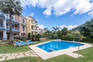Una piscina con sillones de descanso, un camino de piedra y un edificio con balcones.