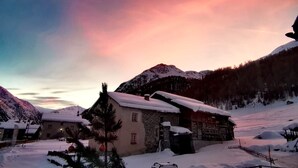 Un villaggio montano innevato con edifici tradizionali, una recinzione in legno e un cielo sereno.