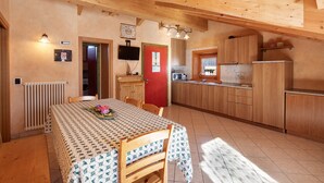 Un interno in legno con un tavolo da pranzo, sedie, una cucina con armadietti in legno, una porta rossa e un televisore.