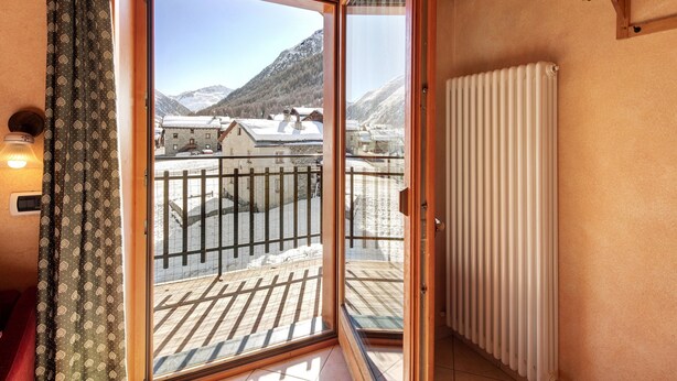 Una stanza con una porta scorrevole in vetro che dà su un balcone con vista sulle montagne innevate.