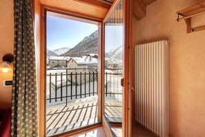 A room with a sliding glass door leading to a balcony with a view of snow-covered mountains.