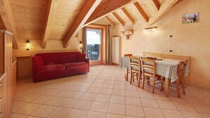 Una stanza accogliente con soffitto in legno, un divano rosso, un tavolo da pranzo con sedie e una finestra con vista.