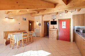 Un intérieur en bois comprenant une table à manger, des chaises, une porte rouge, un coin cuisine avec un four à micro-ondes et un téléviseur fixé au mur.