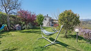 Un patio trasero con césped, una hamaca, una casita de juegos y una casa al fondo.