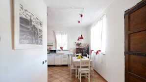 Una cocina con alacenas blancas, una mesa de comedor con sillas, una lámpara colgante roja y una puerta de madera.