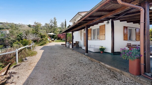 Una casa con entrada de grava, porche de madera y jardín con plantas en macetas.