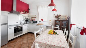 Una cocina con armarios blancos, una pared de acento roja, una mesa de comedor con un centro de frutas y una lámpara colgante roja.