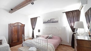 Un dormitorio con cama, armario de madera, una silla, escritorio y lámpara.
