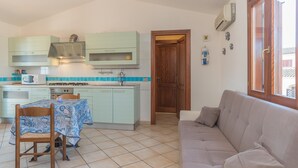 A compact kitchen with a dining table, a sofa, and a wooden door. - Holiday Home 'Trilocale con Ampia Veranda Mare' with A/C & Terrace (san teodoro)