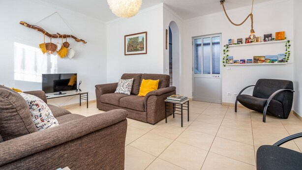 A living room with a sofa, armchairs, a TV, a hanging light fixture, and a bookshelf. - Pet-friendly holiday home 'Casa Quintião' with Wi-Fi (Ferragudo)