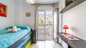 Un dormitorio con cama, escritorio, silla, ventana y balcón.