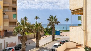 Una calle costera con coches estacionados, palmeras y vista al mar.