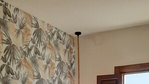 Une chambre à coucher avec un lit, une table de chevet, une lampe, une fenêtre donnant sur un beau paysage et un papier peint aux motifs tropicaux.