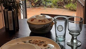 Une table à manger avec des assiettes, un saladier, des verres et des couverts, le tout mis en valeur par un décor de verdure visible à travers une fenêtre.
