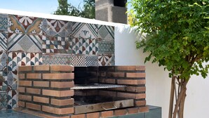 An outdoor brick oven with a tiled backsplash, a metal shelf, and a tree nearby. - Villa Elsa with Pool, Garden, Terrace & Wi-Fi (Conil de la Frontera)