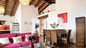 A living room with a red sofa, a glass coffee table, wicker chairs, a dining table, and a red abstract painting on the wall. - Villa Elsa with Pool, Garden, Terrace & Wi-Fi (Conil de la Frontera)