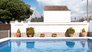 A swimming pool with tiled edges, surrounded by a white wall with a tiled roof, and potted plants. - Villa Elsa with Pool, Garden, Terrace & Wi-Fi (Conil de la Frontera)
