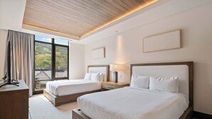 Habitación de hotel con dos camas, un escritorio y un ventanal con vistas al exterior.