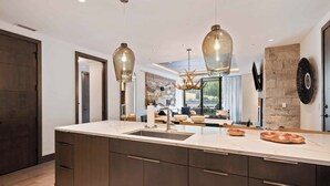 Una cocina moderna con una isla grande, luces colgantes y una pared de acento de piedra.