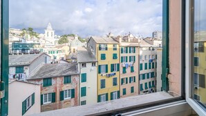 A view from a window overlooking colorful buildings, a bell tower, and a distant church. - GuestHost - Comfortable 40 sqm apartment perfect for 4 guests is located in the heart of the most authentic Genoese historic center, a few steps from Piazza delle Vigne and the church of the same name with the beautiful bell tower that stands out over th (Genova)