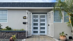 A modern building with a stone-tiled entrance, a gated door, and a small garden area with plants and a palm tree. - Casa Oceana Minutes to Seven Seas Beach + Bio Bay + Marinas (Fajardo)